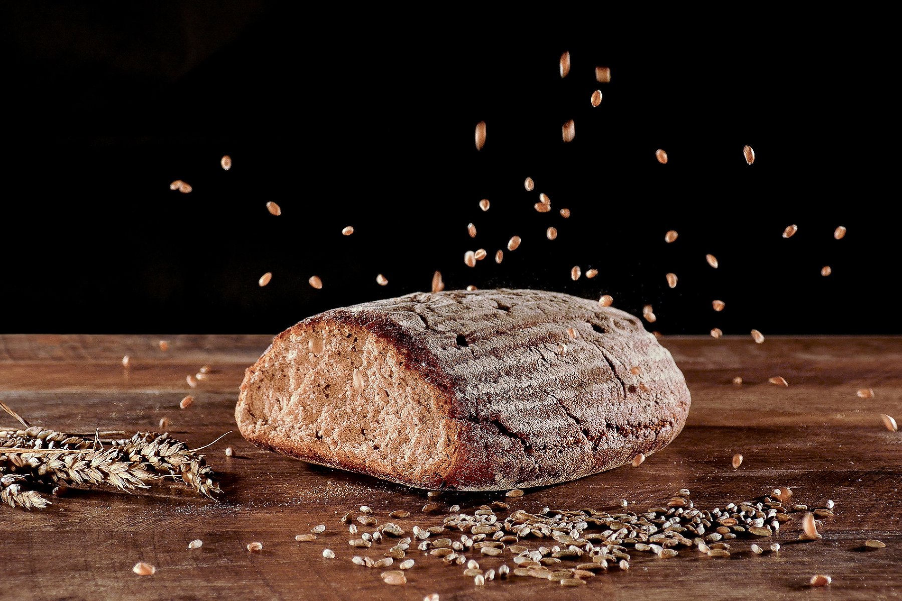Freigestelltes Brot mit fallenden Getreidekörnern, Produktfotografie für die Bäckerei Eisinger