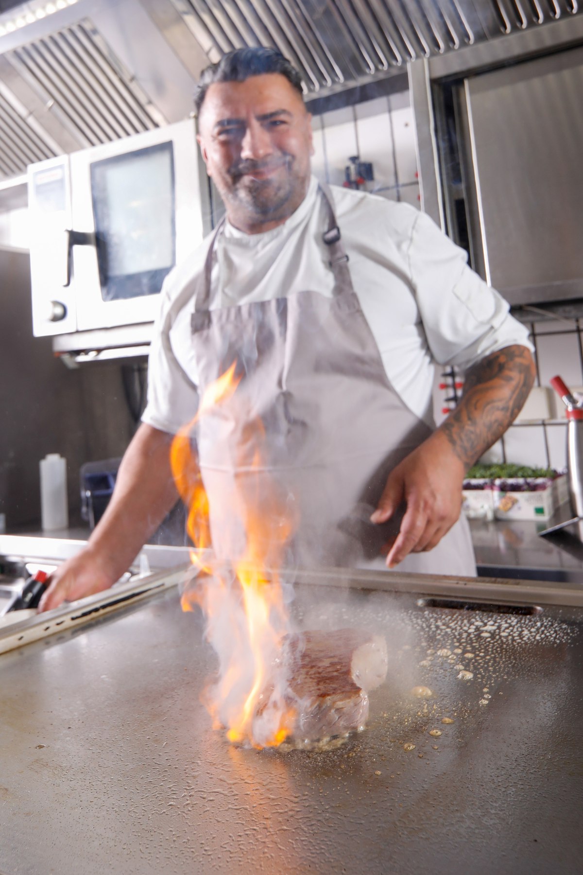 Koch flambiert ein Steak mit der Zange, dramatische Flammen