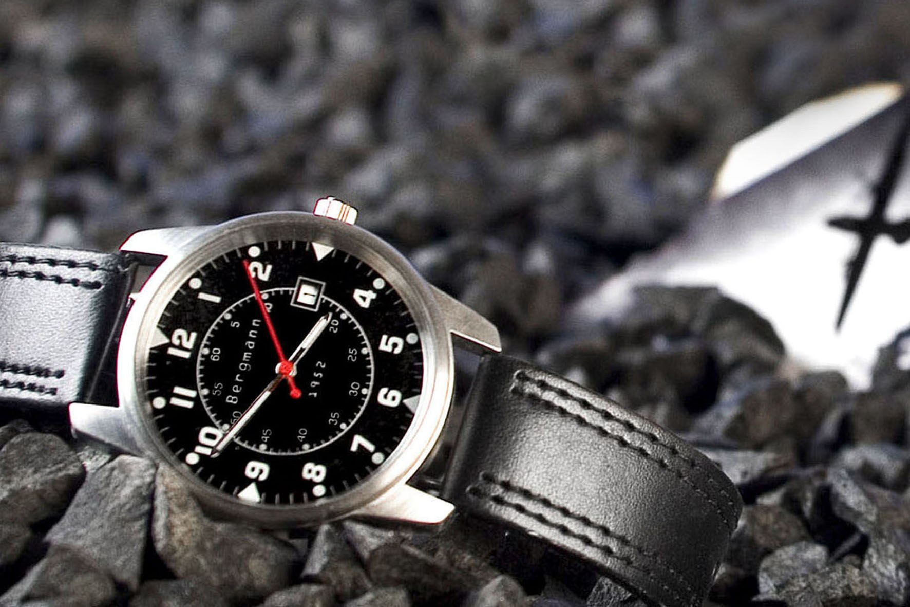 Herrenuhr Bergmann 1952 in Makroaufnahme auf Schotter, dramatisches Bokeh