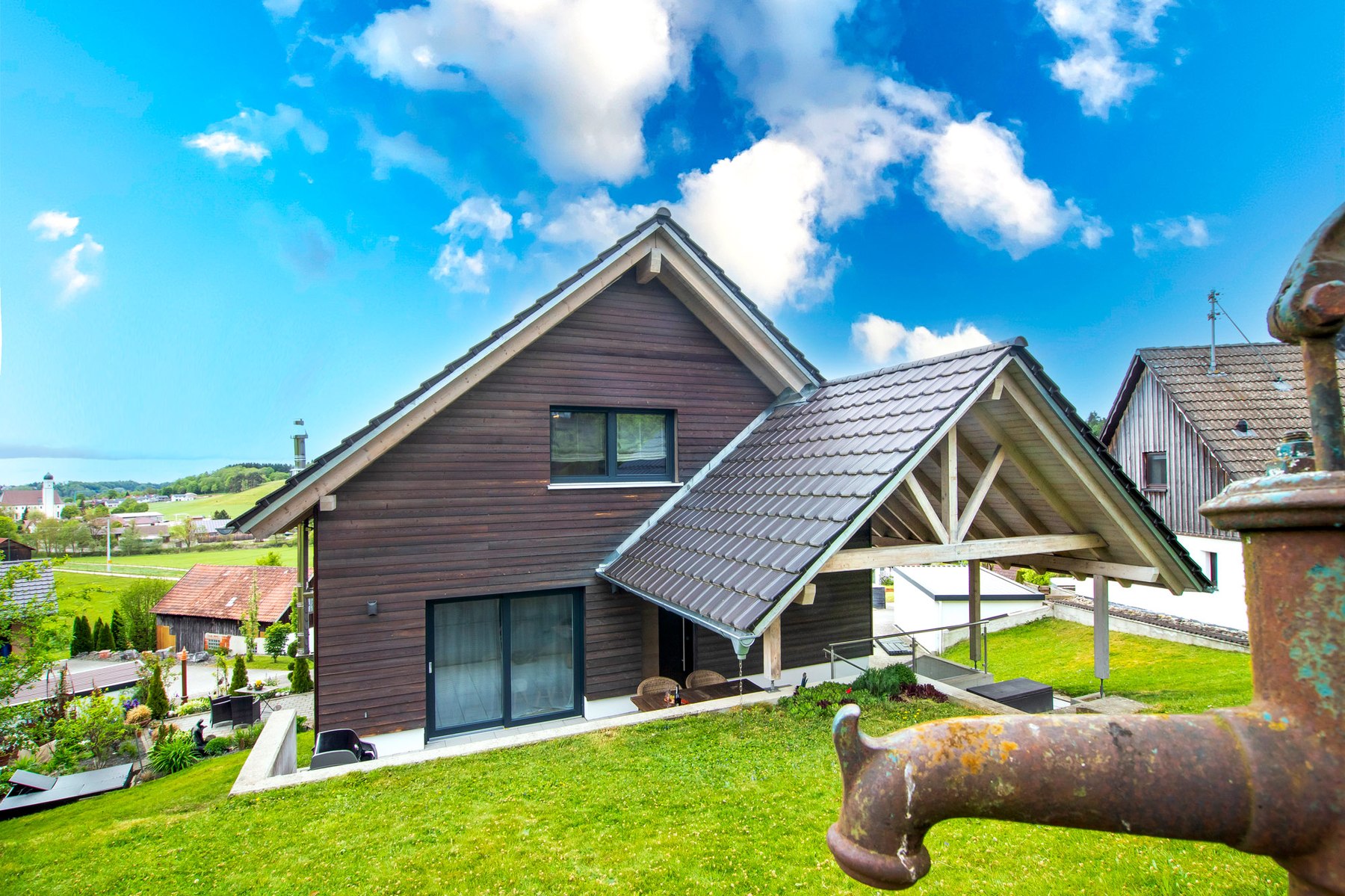 Einfamilienhaus, Holzfassade und Satteldach, mit Handbrunnen im Vordergrund