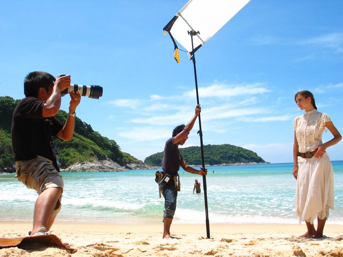 Fotograf, Assistent mit Reflektor und Model am Strand von Phuket